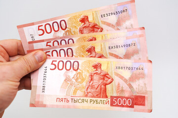 Hand holding three five-thousand ruble banknotes