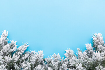 Green artificial fir branches covered with hoarfrost and white snow on light blue table background. Pastel color. Closeup. Empty place for text. Top down view.