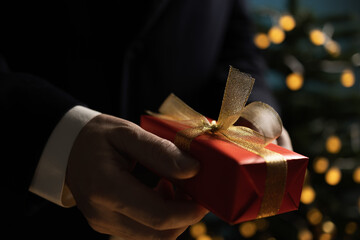 Businessman holding Christmas gift near tree