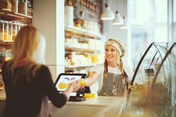 Caucasian female bakery employee serving customer in modern shop interior.