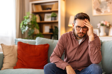 Obraz premium Closeup of man suffering from headache at home, touching his temples, copy space, blurred background. Migraine, headache, stress, tension problem, hangover concept