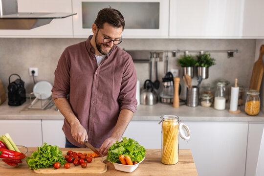 Handsome young man man stand at modern kitchen chop vegetables prepare fresh vegetable salad for dinner or lunch, young male cooking at home make breakfast follow healthy diet, vegetarian concept
