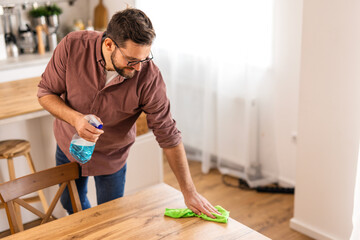 A man is cleaning a table at home, wiping down the surface to maintain a clean and organized space. The image captures a moment of home upkeep and attention to cleanliness in a cozy, everyday setting. © Graphicroyalty