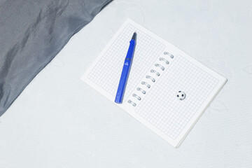 Small soccer ball next to a pen on a blank notebook on a white bedspread
