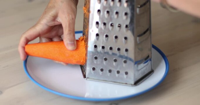 Close-up of a fresh carrot being grated on a stainless steel multi-sided grater over a plate. Concept of healthy food preparation, vitamins, beta-carotene, and natural nutrition. No audio.