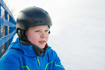 Young snowboarder caucasian boy in black helmet and blue jacket, standing outdoors on a snowy day. This is excited before winter sports adventure.