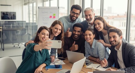 Diverse business team in modern office taking a cheerful group selfie during a productive meeting with laptops, coffee cups, and creative collaboration in bright workspace