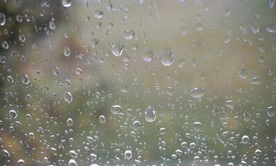 Abstraktes Motiv mit Regentropfenmuster auf Glasscheibe vor Garten bei Regen am Nachmittag im Herbst