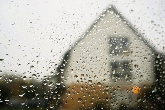 Abstraktes Motiv mit Regentropfenmuster auf Glasscheibe vor Einfamilienhaus mit Spitzdach und wei&szlig;em Himmel mit Licht bei Regen und Sturm am Morgen im Herbst