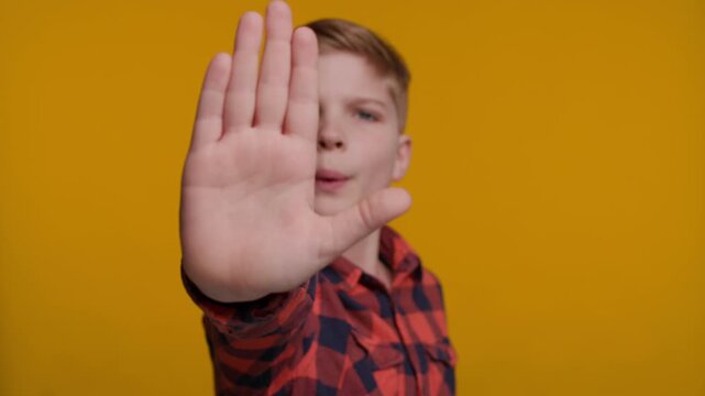 Boy Shows Stop Gesture at Camera on Yellow Background