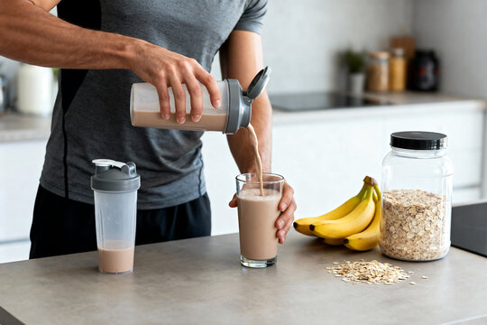Fit man pouring protein shake after morning workout with bananas, oats, and whey powder jar, fitness nutrition and healthy lifestyle in natural light