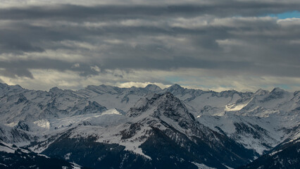 Moody alpine landscape with layered snow-covered mountains under a dramatic cloudy sky in the Austrian Alps. The shifting light and distant peaks convey depth and atmosphere.