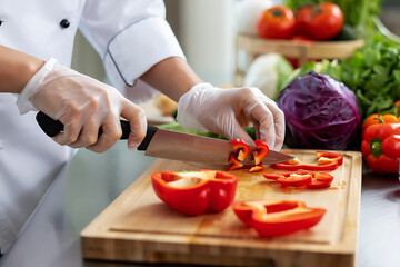 Chef slicing red bell pepper on a cutting board with various vegetables in the background