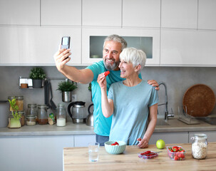 Portrait of a senior mature couple having a healthy breakfast and taking making a selfie with a smart phone mobile phone after fitness exercise training in the morning at home