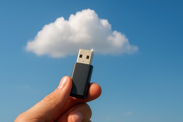 Hand holds USB flash drive against bright blue sky with fluffy cloud, symbolizing cloud storage and technology