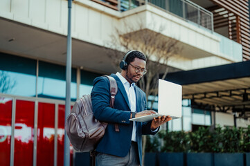 Black businessman working on laptop outdoors wearing headphones
