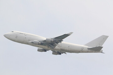 An unmarked, all-white large cargo jet airplane climbing after takeoff against a plain overcast sky.