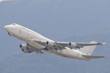 An unmarked, all-white large cargo jet airplane climbing after takeoff against a plain overcast sky.
