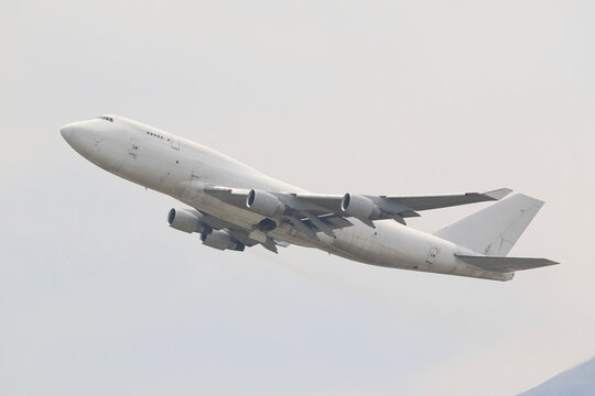 An unmarked, all-white large cargo jet airplane climbing after takeoff against a plain overcast sky.