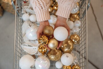 A detailed view of a shopping cart filled with golden and white Christmas ornaments, capturing holiday shopping and decoration preparation in a festive retail environment.