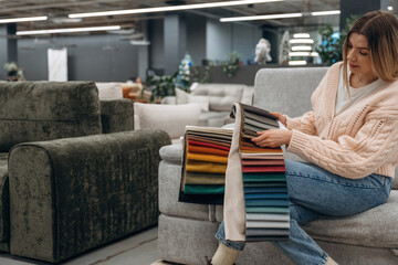 Obraz premium Woman Choosing Fabric Swatches on Sofa in Modern Furniture Store