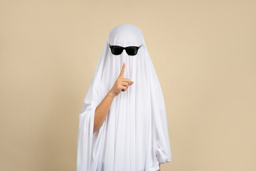Unrecognizable woman in white ghost costume with scary pose on beige background on Halloween.