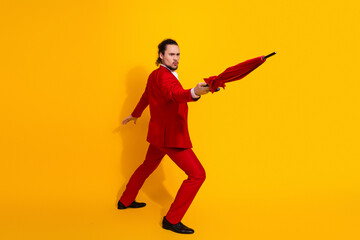 Funky red suited man poses with umbrella in bright yellow studio for bold fashion and comedy vibes