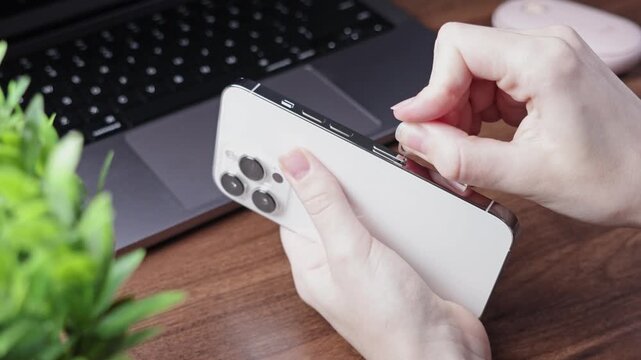 Person's hand expertly inserts a SIM ejector tool into a modern white smartphone's slot, symbolizing essential mobile connectivity and device setup