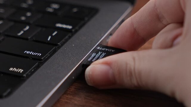 Human hand inserts a black microSD card adapter, labeled microSDHC and microSDXC, into a laptop's slot, enabling crucial data storage and transfer