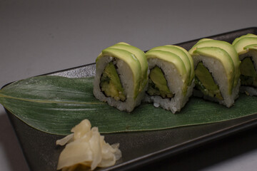 Deliciously sliced sushi rolls, filled with fresh avocado, elegantly arranged on a black plate with a ginger garnish