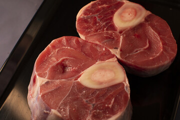 Two individual pieces of raw, fresh meat, complete with bone, are artfully arranged on a sleek black plate