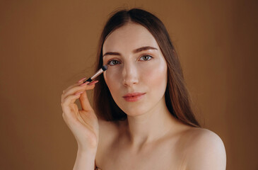 Fototapeta premium Spreads powder on the face. Young woman is against background