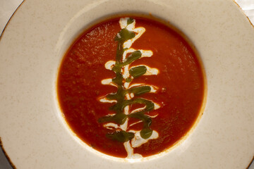 A steaming bowl of rich tomato soup adorned with a beautifully decorative swirl of cream and vibrant green sauce