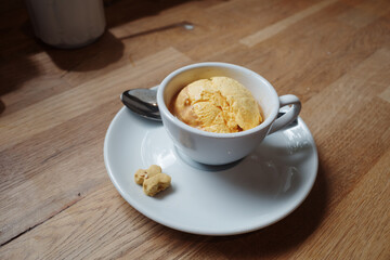 A simple, elegant dessert featuring a single scoop of yellow ice cream or sorbet served in a white coffee cup.