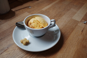 A simple, elegant dessert featuring a single scoop of yellow ice cream or sorbet served in a white coffee cup.