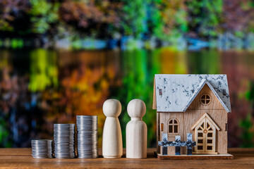 Wooden house toy model, stack of coins and figures of people on nature background. Concept of planning to save money for purchase or construction of a home, mortgage and real estate investment