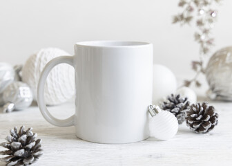 White blank coffee mug near cream Christmas baubles and pine cones closeup, mockup