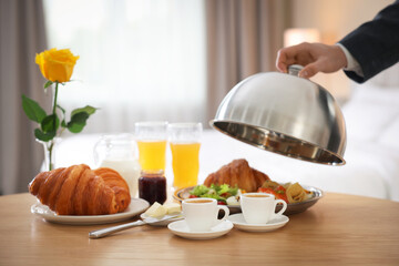 Waiter serving breakfast on wooden table in hotel room, closeup. Space for text