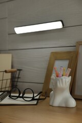 Portable LED light on wall over shelf with decor, notebook and glasses