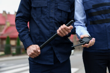 Police officers with radio and baton on city street, closeup