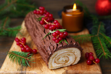 Delicious Yule log (traditional Christmas cake) with redcurrant and fir tree branches on table, closeup