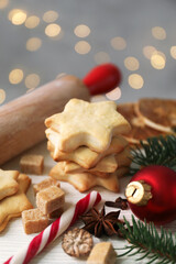 Christmas composition with cookies in shape of stars, spices, bauble and fir tree branches on light wooden table against grey background with blurred lights, closeup