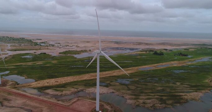 Torre e&oacute;lica girando nos pequenos len&ccedil;&oacute;is maranhenses, mar ao fundo, praia e estrada