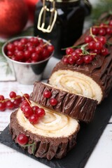 Delicious Yule log (traditional Christmas cake) with redcurrant on light table, closeup