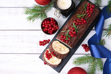 Delicious Yule log (traditional Christmas cake) with redcurrant, decor and fir tree branches on light wooden table, flat lay. Space for text