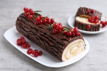 Delicious Yule log (traditional Christmas cake) with redcurrant on gray textured table, closeup