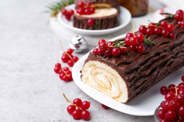 Delicious Yule log (traditional Christmas cake) with redcurrant on gray textured table, closeup. Space for text