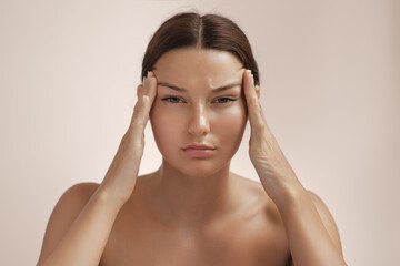 Naklejka premium Stressed Woman Touching Temples And Frowning In Skincare Studio Portrait