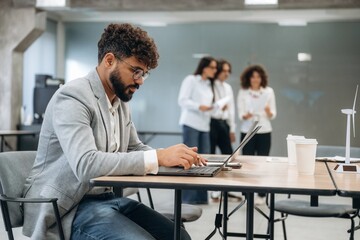 Man in glasses is sitting on the chair. Group of people are working in the office together as a team