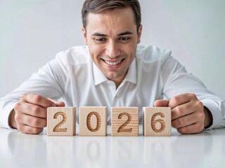 Smiling man arranging wooden blocks with number 2026, concept of new year, business goals, optimism, and fresh beginnings.